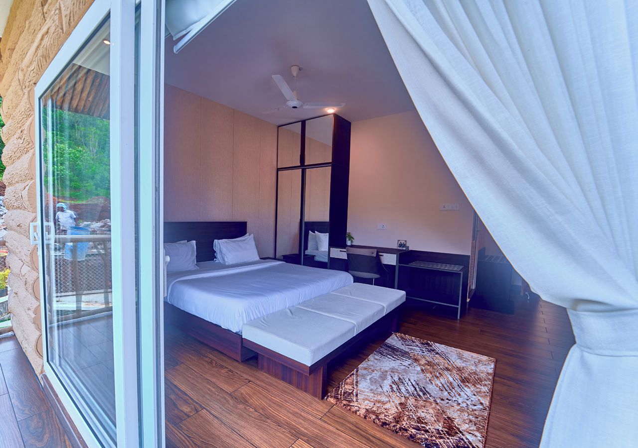 Quarto com uma cama grande, uma escrivaninha e vista através de uma porta de vidro.