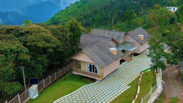 A two-story house with a sloped roof, a balcony, and a paved driveway. - The Treetop Escape by VOYE HOMES (Peermade)
