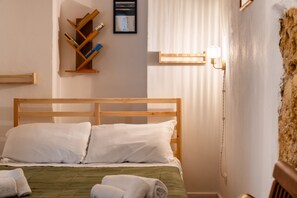 Ein Hotelzimmer mit einem hölzernen Bett, weißen Kissen, einer grünen Bettdecke, einem hölzernen Bücherregal mit Büchern, einem gerahmten Bild an der Wand und einer Leuchte.