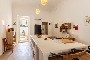 Eine kompakte Küche mit einer zentralen Kochinsel, einem Esstisch und Stühlen. Es gibt einen Kühlschrank, eine Spüle und ein Fenster mit Blick auf Grünflächen.