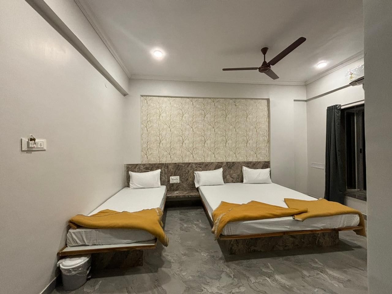 A hotel room with two beds, a ceiling fan, and a marble-patterned wall.