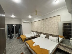 A hotel room with three beds, a ceiling fan, a marble wall, and a sliding door. - Hotel Grand Vrundavan (Akalkot)