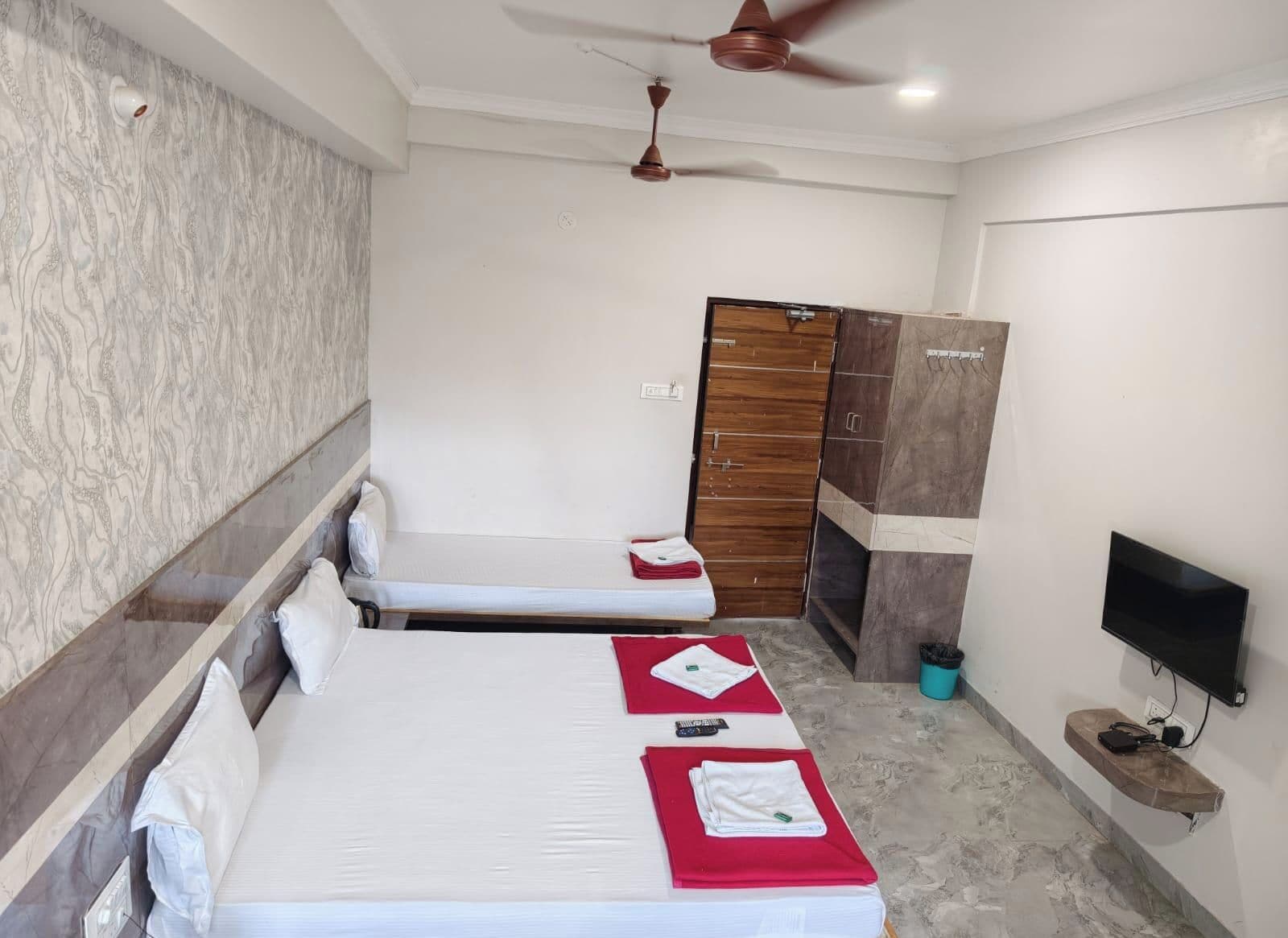 A hotel room with two single beds, a wardrobe, a television, and a ceiling fan.