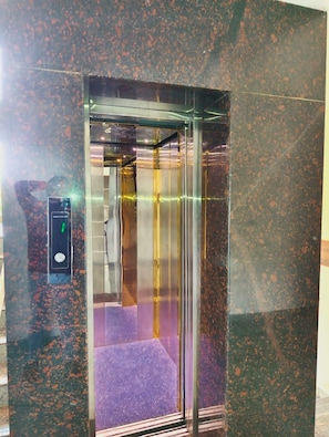 An elevator with a control panel and a purple carpeted interior.