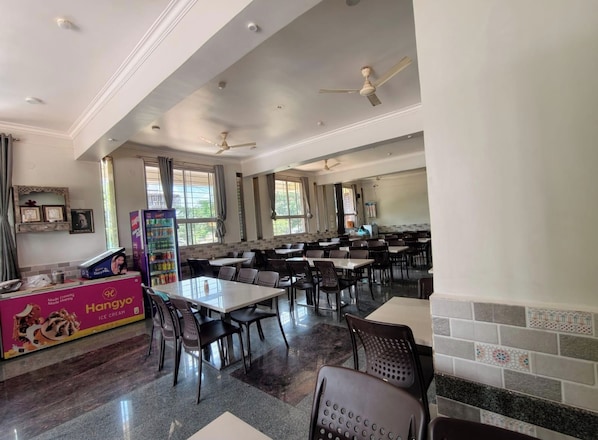 A dining area with tables and chairs, ceiling fans, and a vending machine.