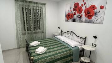 Een slaapkamer met een bed, een nachtkastje, een wandlamp en een schilderij van rode bloemen.