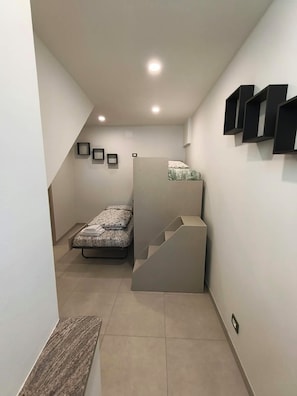 A compact room with a bed, a staircase, and a wall-mounted shelf unit.