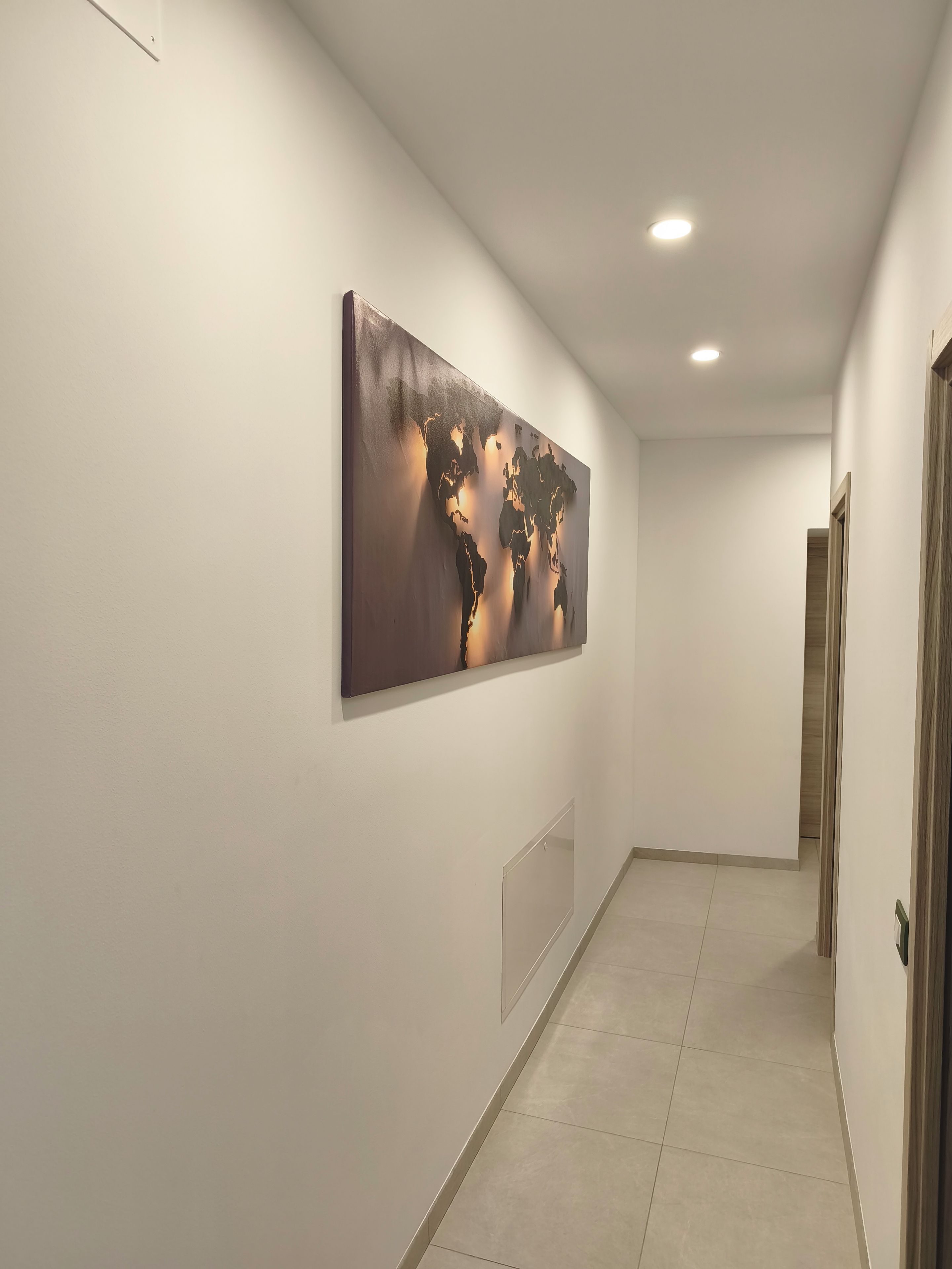 A hallway with a world map artwork on the wall, a recessed ceiling light, and a door at the end.