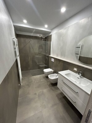 Un bagno moderno con doccia, WC, bidet e un mobile lavabo con specchio.