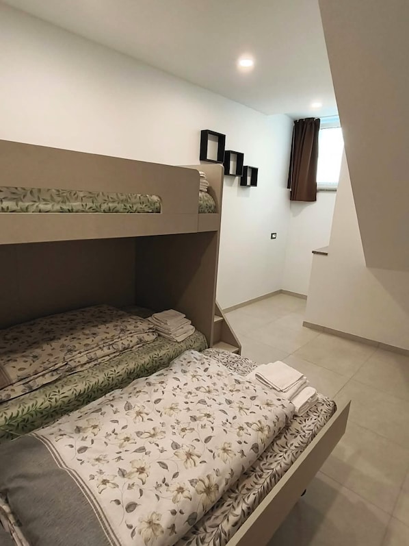 A bunk bed with floral bedding, a small shelf with framed pictures, and a window with curtains.