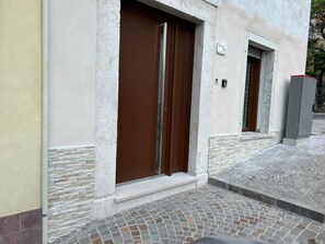 L’entrée d’un immeuble, avec une porte marron et une petite marche menant à un trottoir carrelé.