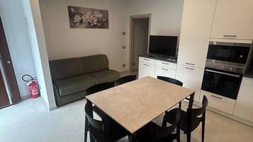 Een moderne keuken met een eettafel, stoelen, een bank en een flatscreen televisie.