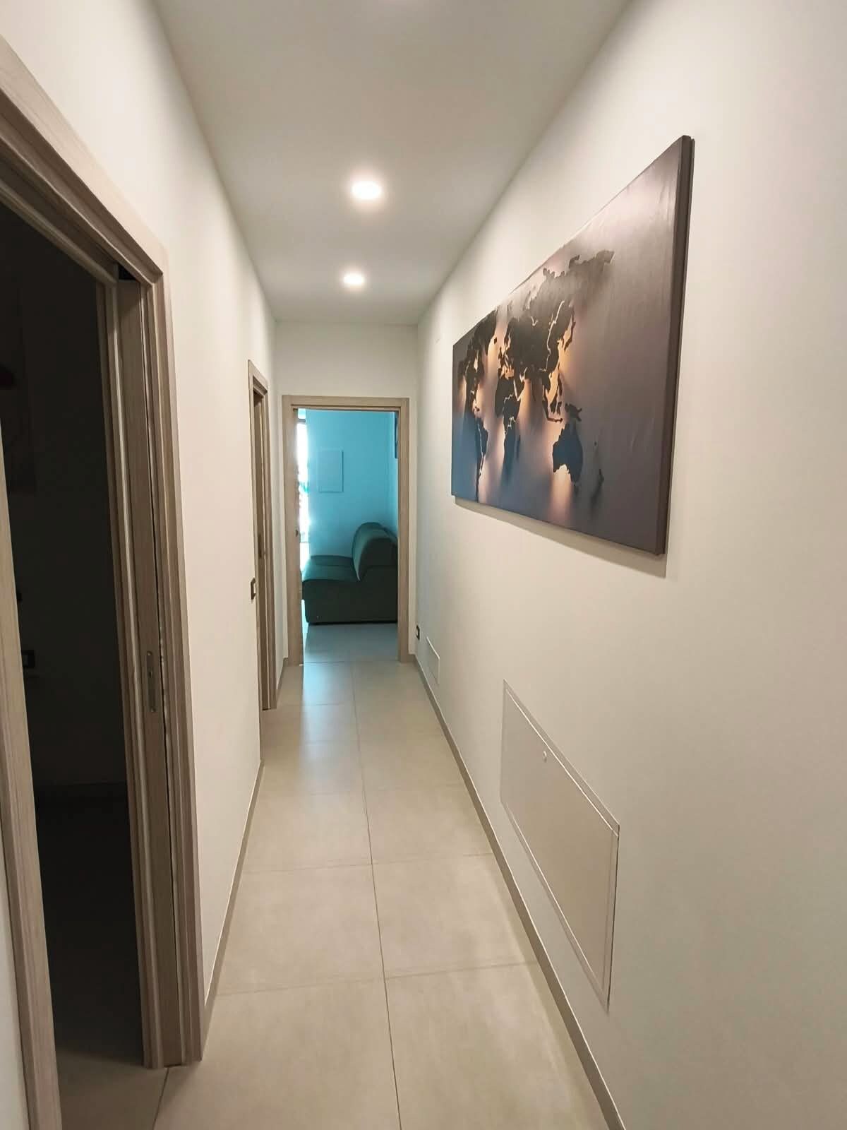 A hallway with a large abstract painting on the wall, a door on the left, and a room visible in the distance.