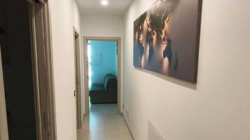 A hallway with a large abstract painting on the wall, a door on the left, and a room visible in the distance.