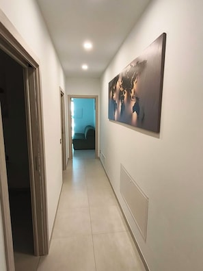 A hallway with a large abstract painting on the wall, a door on the left, and a room visible in the distance.