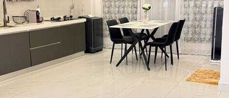 A modern kitchen with a dining area, featuring a white tiled floor, a central island, and contemporary appliances.