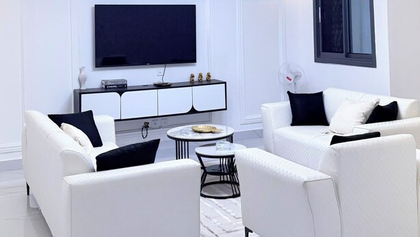 Un soggiorno moderno con divani bianchi, una TV a schermo piatto e un soffitto con illuminazione a incasso.