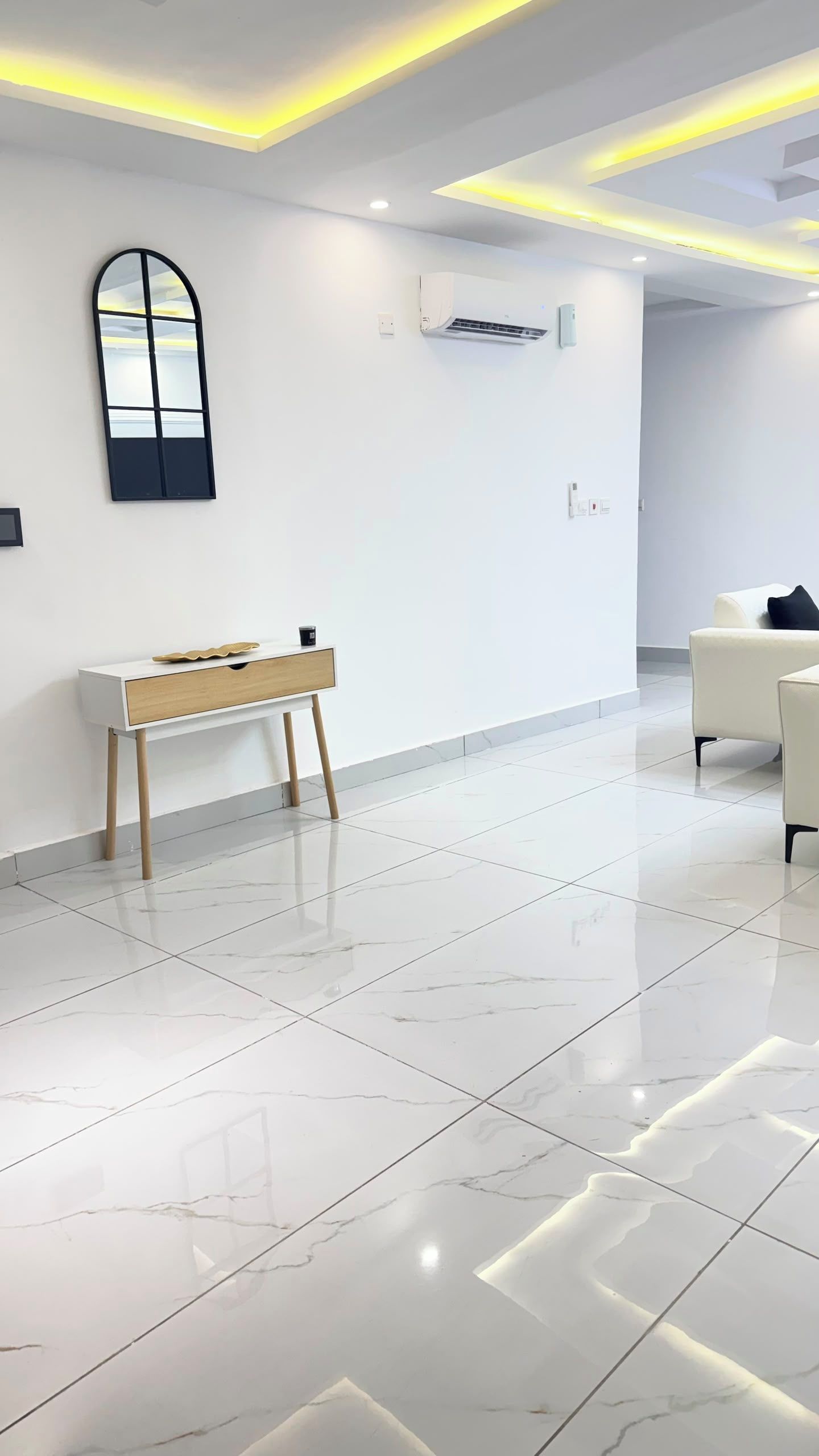 Un intérieur moderne avec une console blanche, un canapé et un grand miroir mural.