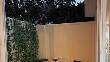 Een terras buiten met een ronde tafel en twee stoelen, een hangplant en een lantaarn.