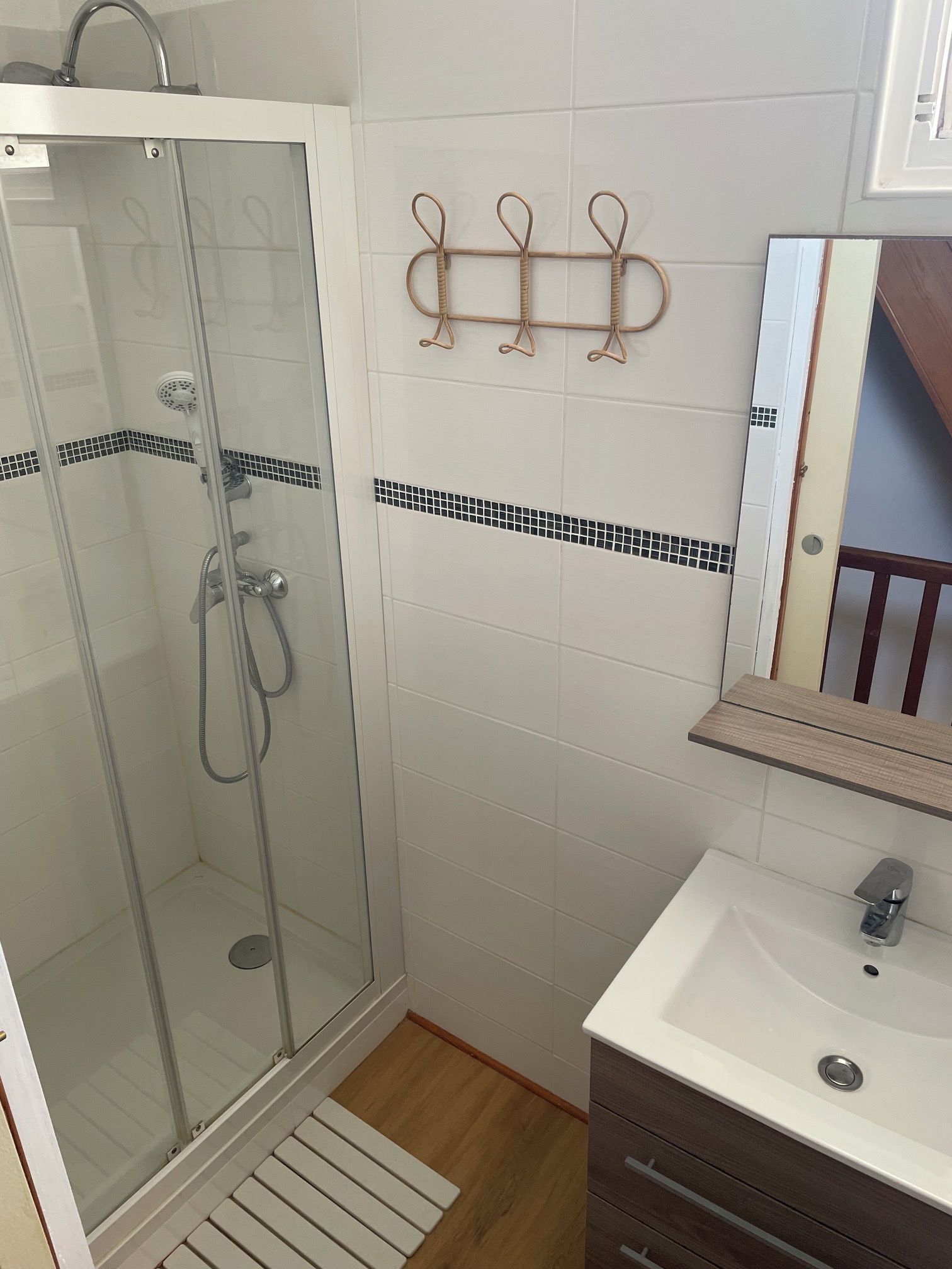 Casa de banho com cabine de duche em vidro, lavatório com espelho e porta-toalhas.