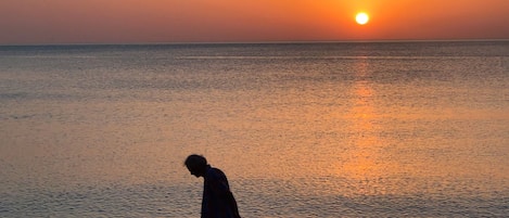 A person walking along a pebbly beach during sunset.