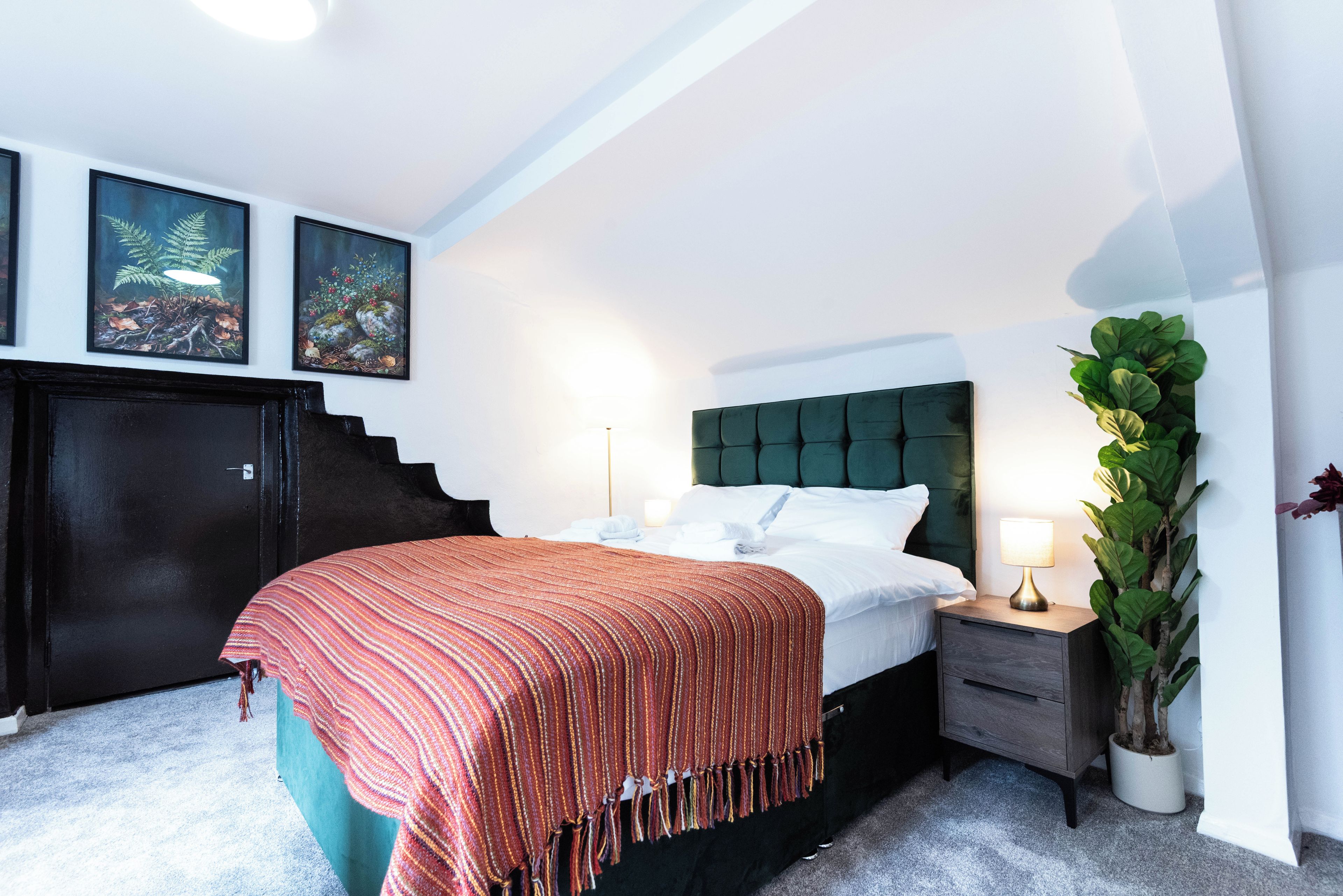 A bedroom with a bed, nightstand, lamp, and a potted plant.