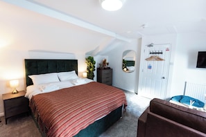 A hotel room with a bed, a nightstand, a dresser, a mirror, a coat rack, and a door with a fire safety sign. - The Stanley Arms Hotel by Guestz (Seascale)