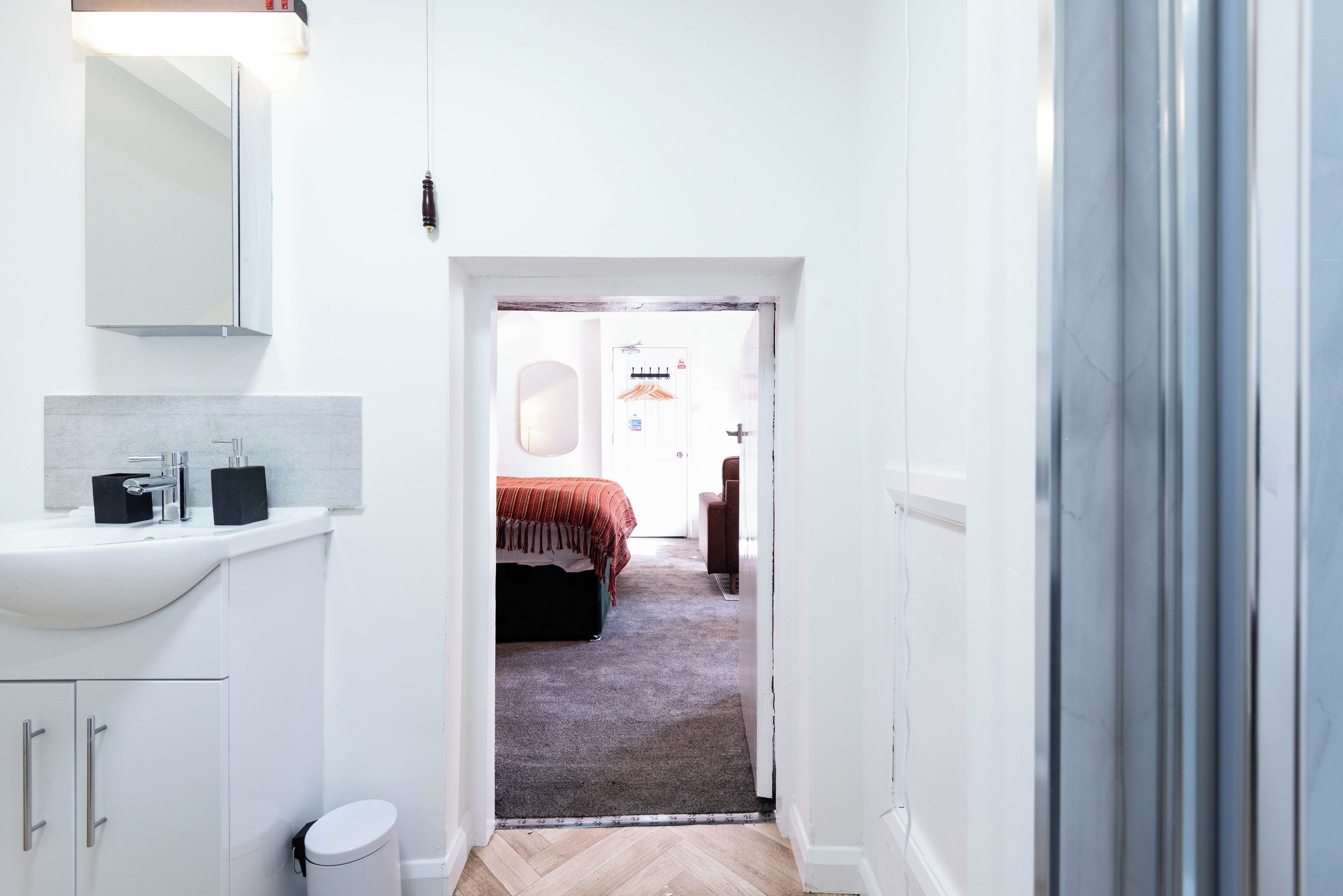 A narrow hallway leading to a bedroom with a bed, a bedside table, and a mirror.