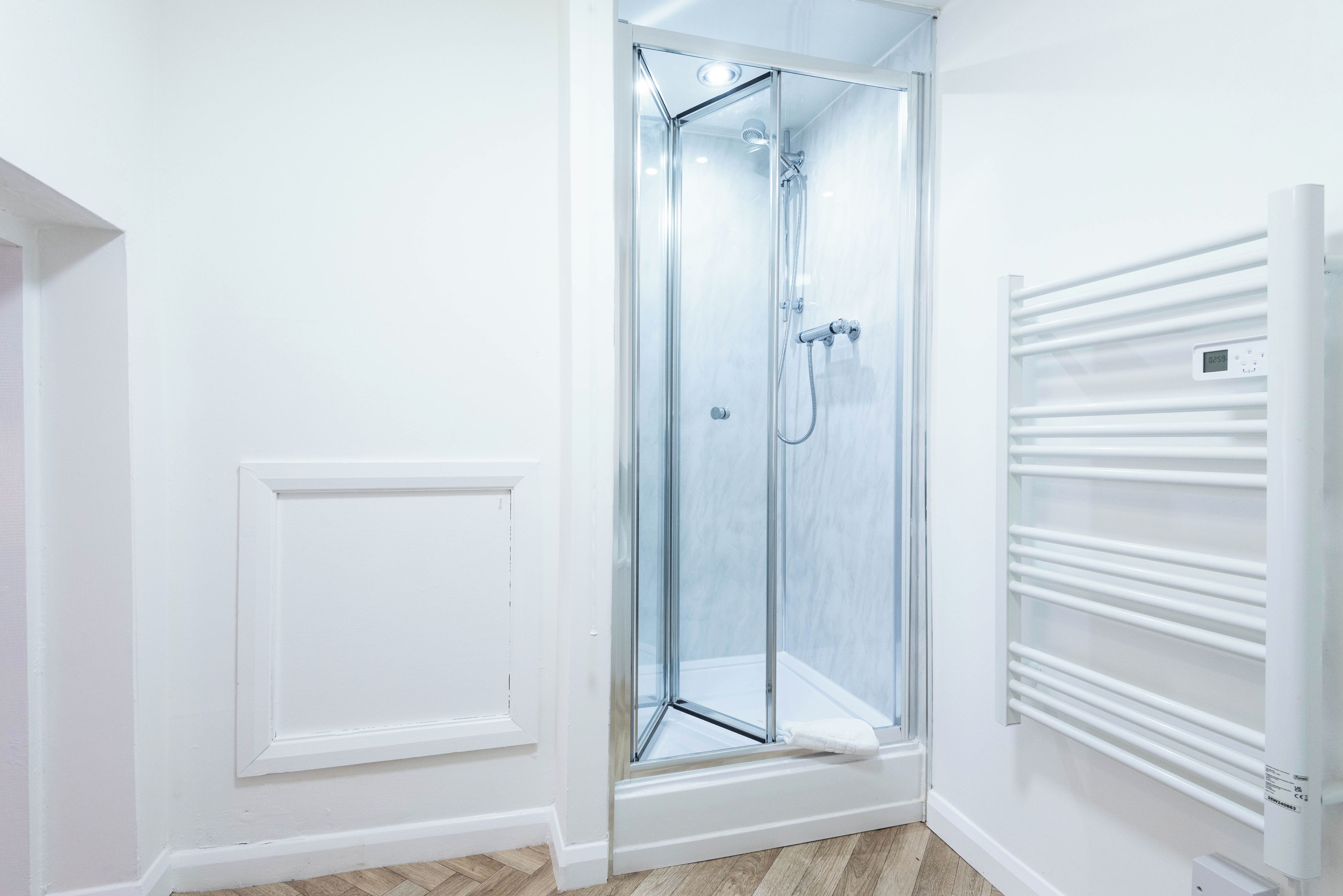 A modern bathroom with a glass shower enclosure, a white radiator, and a wooden floor.