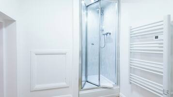 A modern bathroom with a glass shower enclosure, a white radiator, and a wooden floor.