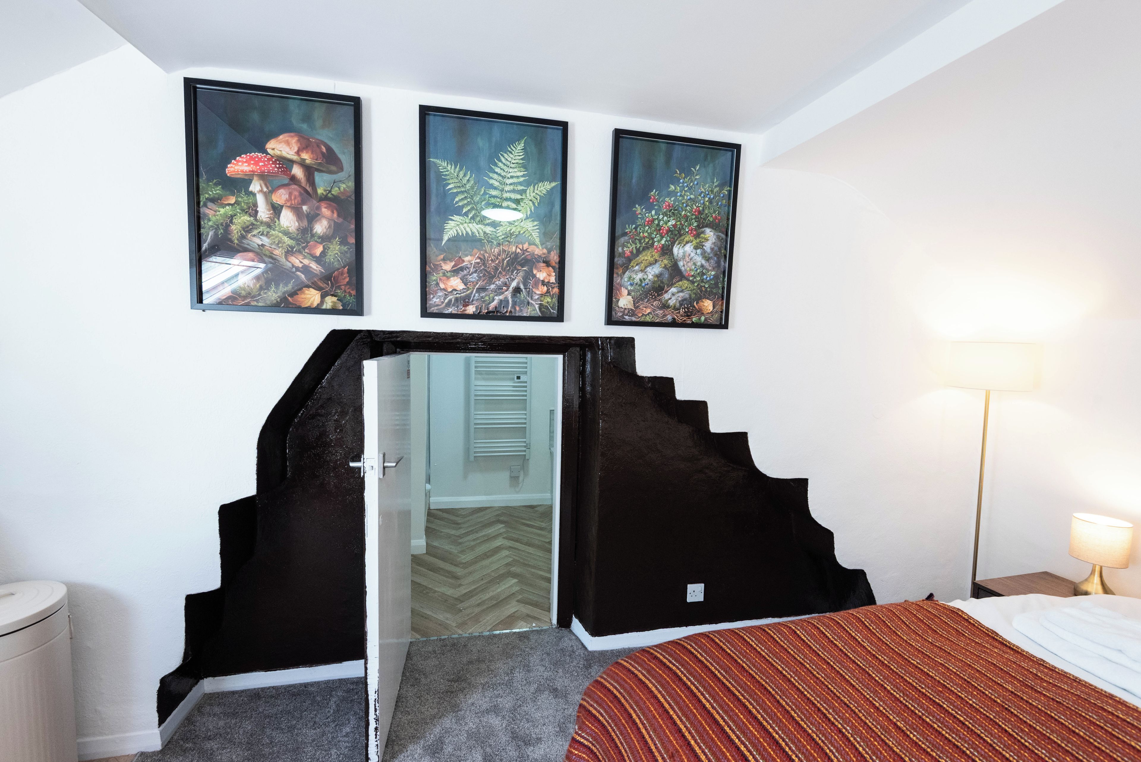 A hotel room with a bed, a nightstand, a lamp, and three framed pictures on the wall.