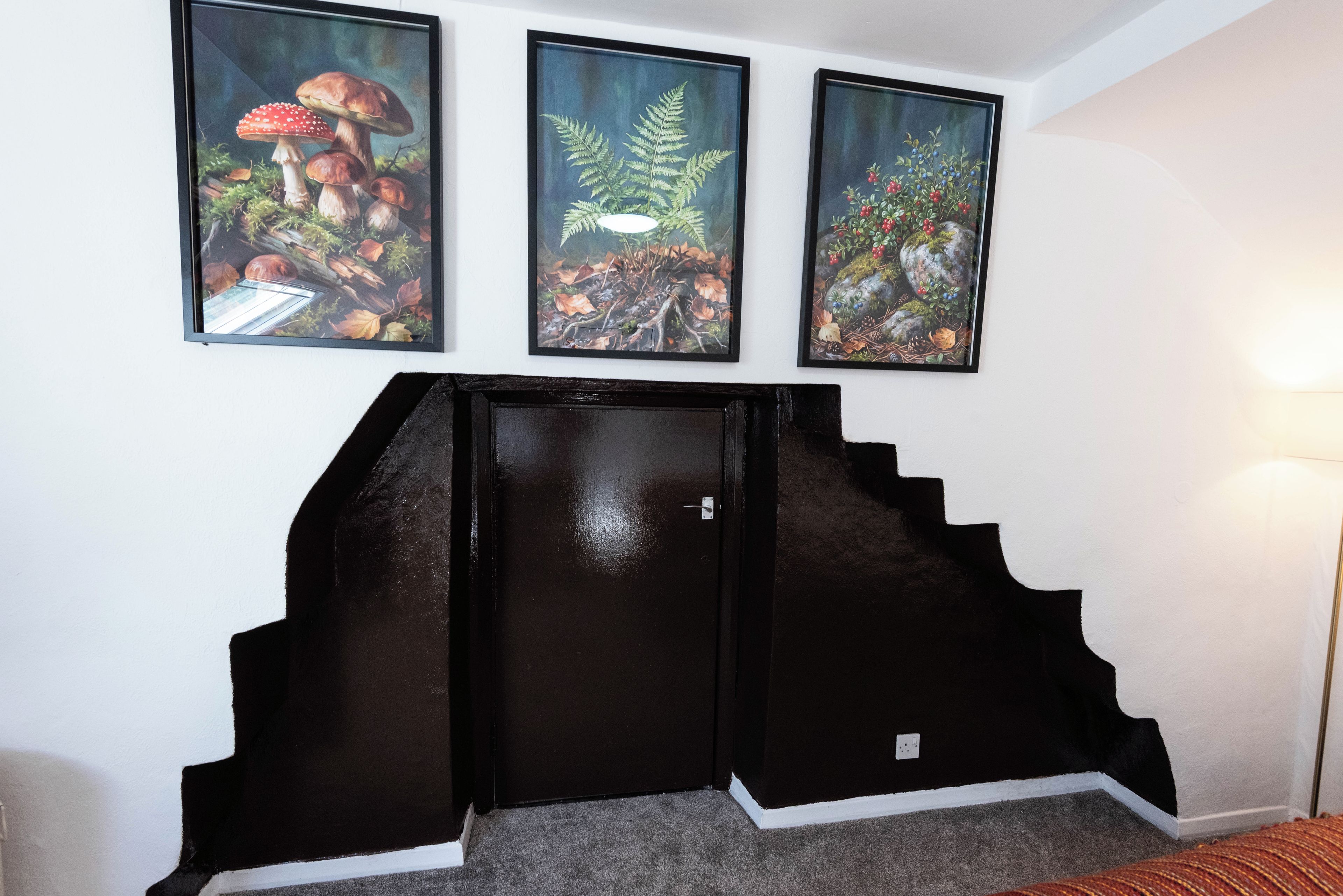 A staircase with a black handrail and a door, leading to a room with a white wall.