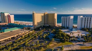 A coastal hotel complex with multiple high-rise buildings, a parking area, and a beach view. - Pelican Beach 1516 2 Bedroom Condo (Destin)