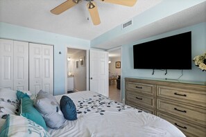 Ein Schlafzimmer mit einem Bett, einem Schminktisch, einem Fernseher und einem Deckenventilator.