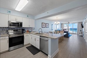 A modern kitchen with stainless steel appliances, a dining area with a view, and a living room with a balcony. - Pelican Beach 1516 2 Bedroom Condo (Destin)