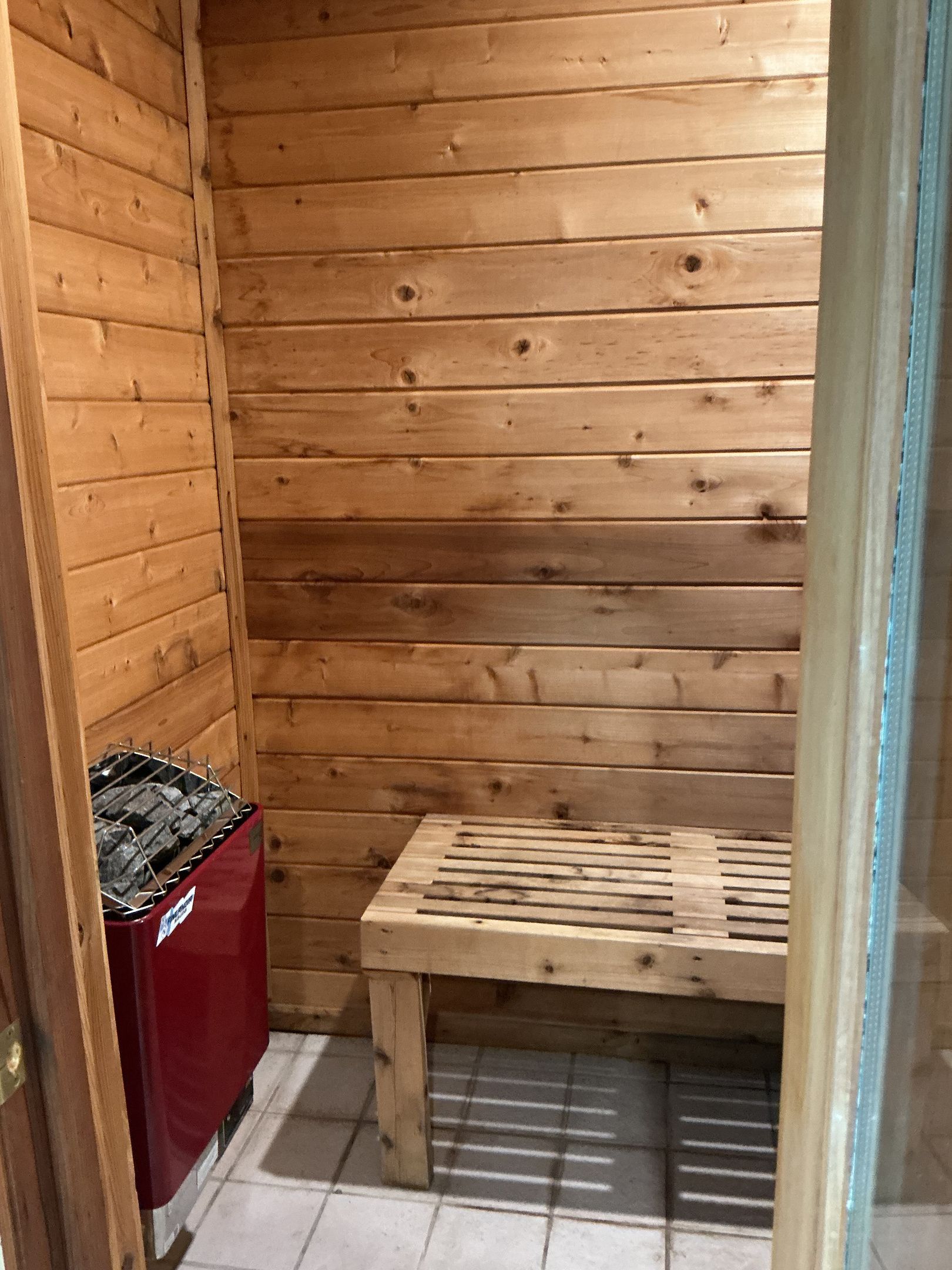 Et træs sauna med bænk og rød saunaovn.