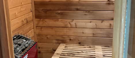 Et træs sauna med bænk og rød saunaovn.