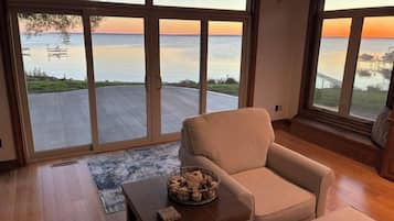A room with a large sliding glass door leading to a deck, a beige armchair, a small wooden table, and a basket of items.