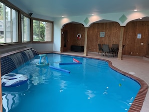 Une piscine intérieure agrémentée d’une cascade, un espace détente avec des fauteuils et une vue sur l’extérieur grâce à de grandes fenêtres.