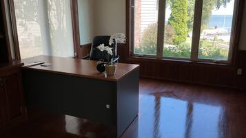 Une pièce comprenant un bureau en bois, une chaise et une grande fenêtre donnant sur un paysage verdoyant et un plan d’eau.
