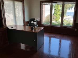 A room with a wooden desk, a chair, and a large window with a view of greenery and a body of water.