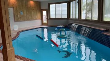 Une piscine intérieure avec un mur en bois, une vue sur la mer et un bord orné de carreaux bleus.