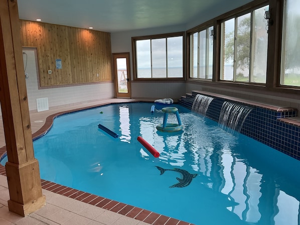 An indoor swimming pool with a wooden wall, a view of the sea, and a blue tiled edge.