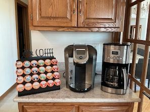 Un comptoir de cuisine avec une machine à café, une cafetière et une sélection de capsules de café.