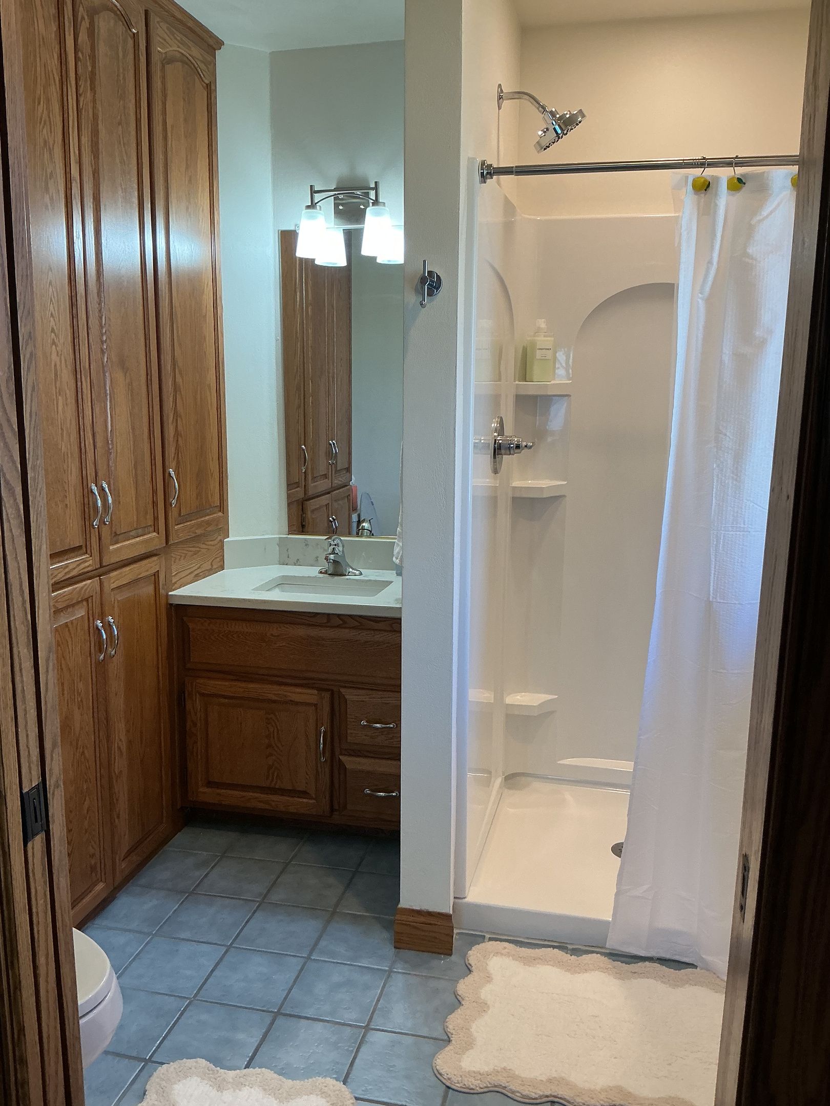 Une salle de bain avec des meubles en bois, un lavabo, une douche avec une porte en verre et des toilettes.