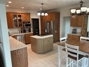 A kitchen with wooden cabinets, a central island, a dining table with chairs, and pendant lighting.