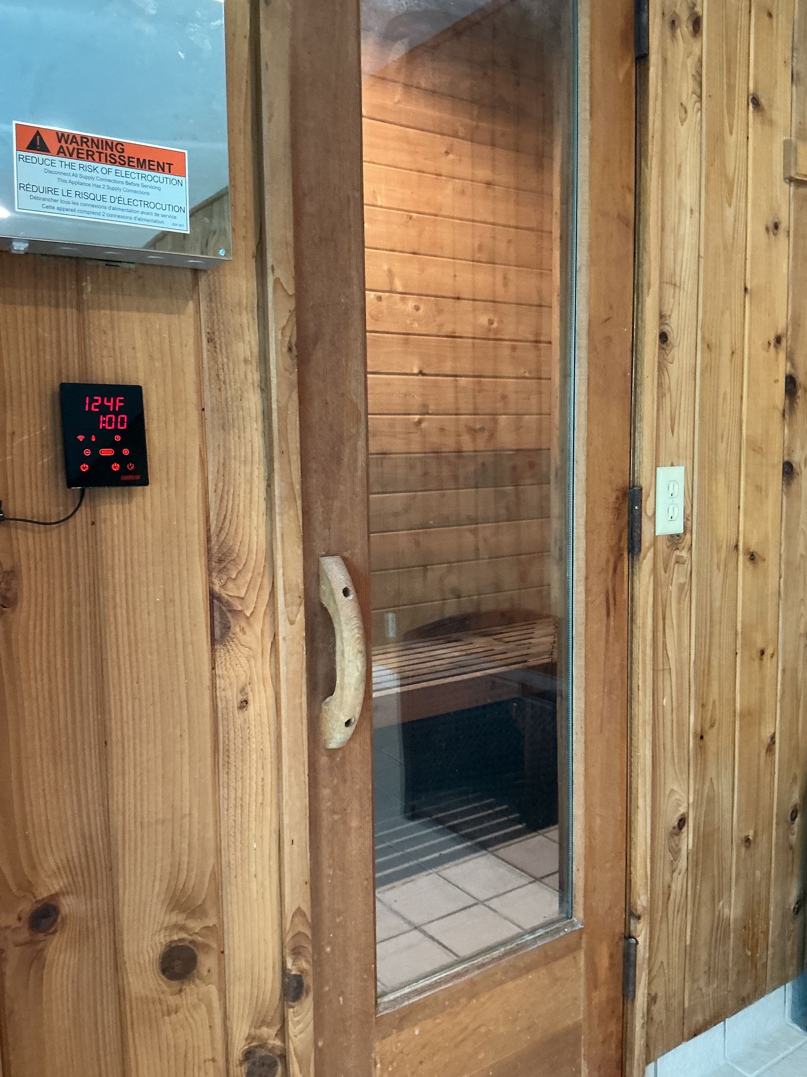 A wooden door with a digital thermostat displaying 24 degrees Celsius and 100% humidity.