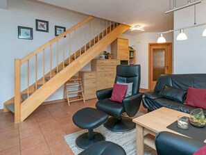 A living room with a wooden staircase, a black leather sofa, a wooden coffee table, and a small plant on the table. - 7/t5 Holiday Home Park \"freesenbruch\" (Zingst)