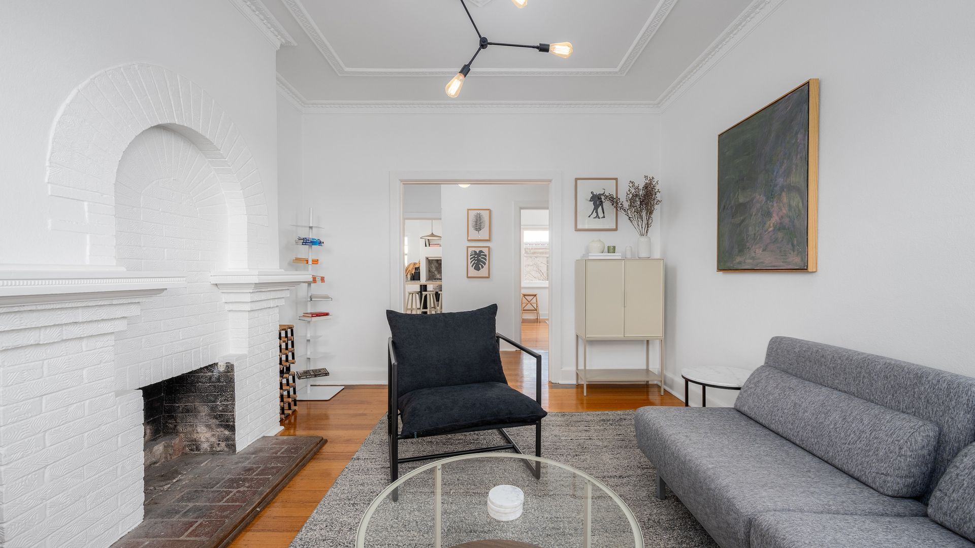 A living room with a fireplace, a grey sofa, a black armchair, and a painting on the wall.
