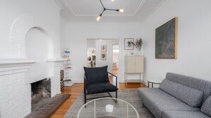 Ein Wohnzimmer mit Kamin, einem grauen Sofa, einem schwarzen Sessel und einem Gemälde an der Wand.